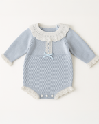 Body azul para bebê em tricô com gola rendada branca e laço decorativo azul claro, combinando delicadeza com sofisticação.