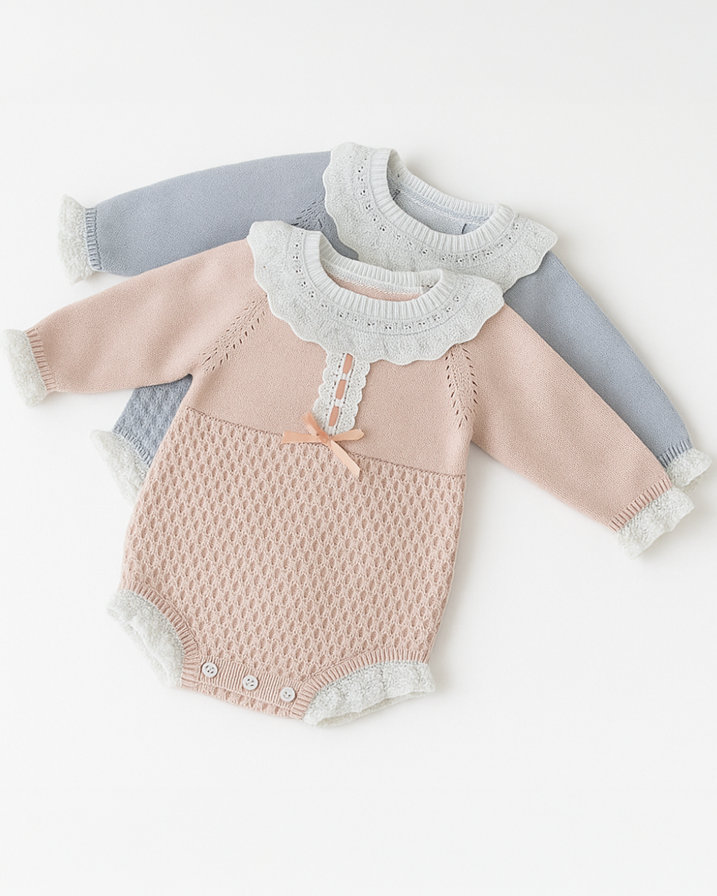 Dois bodies de bebê em tricô nas cores rosa e azul, com gola de babado branca e punhos delicados, ideais para o inverno.