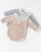 Dois bodies de bebê em tricô nas cores rosa e azul, com gola de babado branca e punhos delicados, ideais para o inverno.