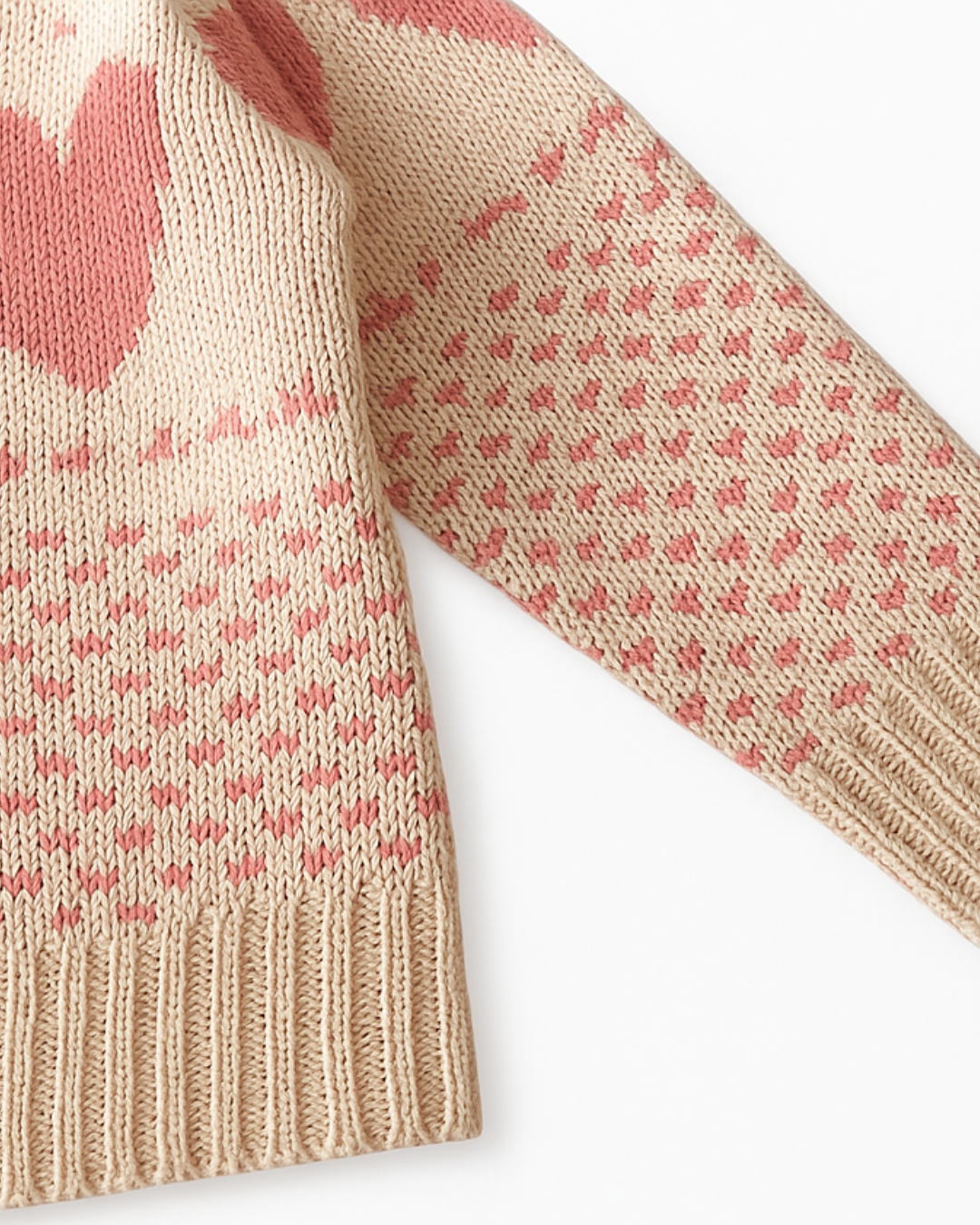 Detalhe da alça com botão do macacão infantil de tricô, com estampa de corações rosa sobre fundo bege.