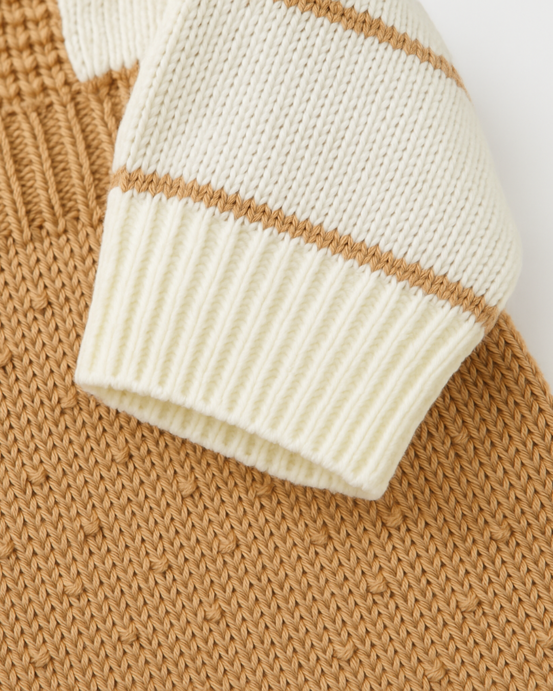 Detalhe da manga listrada em tricot bege e creme de macacão infantil